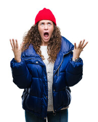 Sticker - Beautiful young brunette curly hair girl wearing winter coat, wool cap and sweater over isolated background crazy and mad shouting and yelling with aggressive expression and arms raised. Frustration