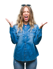 Canvas Print - Beautiful young blonde woman wearing sunglasses over isolated background celebrating mad and crazy for success with arms raised and closed eyes screaming excited. Winner concept