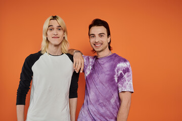 Wall Mural - Two young friends in stylish attire, pose against a vibrant orange backdrop.