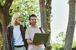 © Bliss - Two young friends, dressed casually, walk through a wooded area. One is holding a laptop.