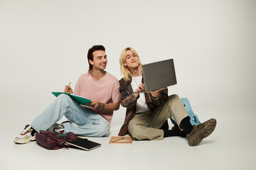 Wall Mural - Two young queer students work on a project together, one using a laptop while the other takes notes.