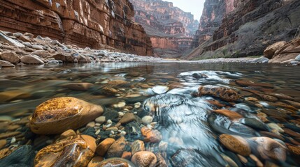 A clear river flowing over smooth stones in a deep canyon, with steep rock walls rising on either side.