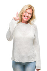 Wall Mural - Middle age blonde woman wearing winter sweater isolated background pointing finger up with successful idea. Exited and happy. Number one.