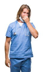 Canvas Print - Young handsome doctor man with long hair over isolated background smelling something stinky and disgusting, intolerable smell, holding breath with fingers on nose. Bad smells concept.