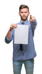 Sticker - Young handsome man holding blank paper over isolated background pointing with finger to the camera and to you, hand sign, positive and confident gesture from the front