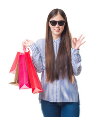 Wall Mural - Young Chinese woman over isolated background holding shopping bags on sales doing ok sign with fingers, excellent symbol