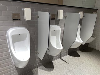 Interior of modern restroom with white wall and warm light. Row of sanitary ware with men urinals in public toilet.