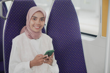 Wall Mural - A smilling woman sitting on a train using cell phone