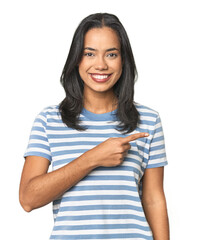 Wall Mural - young latina posing in studio smiling and pointing aside, showing something at blank space.