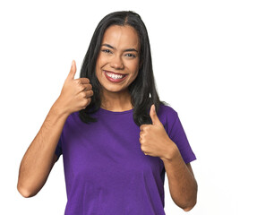 Wall Mural - young latina posing in studio raising both thumbs up, smiling and confident.