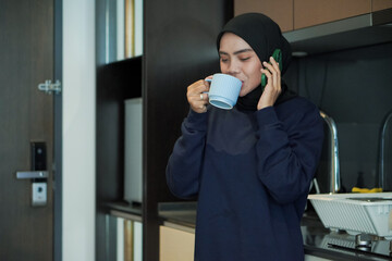 Wall Mural - A woman is smiling and holding a cup of coffee while holding a cell phone. Concept of relaxation and enjoyment, as the woman is taking a break from her daily routine to enjoy a warm beverage