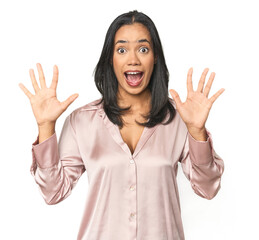 Wall Mural - simple portrait of a young latina receiving a pleasant surprise, excited and raising hands.