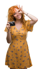 Wall Mural - Young redhead woman taking pictures holding vintage camera with happy face smiling doing ok sign with hand on eye looking through fingers