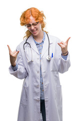 Canvas Print - Young redhead woman wearing doctor uniform shouting with crazy expression doing rock symbol with hands up. Music star. Heavy concept.