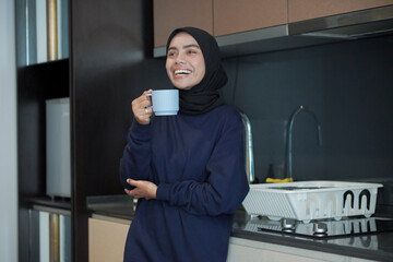 Wall Mural - A woman is smiling and holding a cup of coffee. Concept of relaxation and enjoyment, as the woman is taking a break from her daily routine to enjoy a warm beverage.