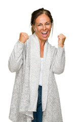 Poster - Beautiful middle age adult woman wearing winter sweater over isolated background very happy and excited doing winner gesture with arms raised, smiling and screaming for success. Celebration concept.