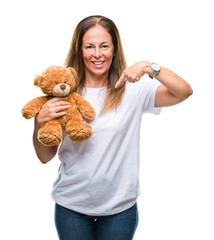 Poster - Middle age hispanic woman holding cute teddy bear plush over isolated background with surprise face pointing finger to himself