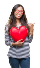 Sticker - Young asian woman in love holding read heart over isolated background pointing and showing with thumb up to the side with happy face smiling