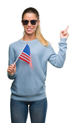 Wall Mural - Beautiful young woman holding USA flag very happy pointing with hand and finger to the side