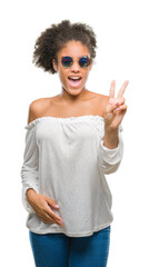 Wall Mural - Young afro american woman wearing sunglasses over isolated background smiling with happy face winking at the camera doing victory sign. Number two.