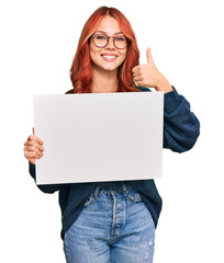 Poster - Young redhead woman holding blank empty banner smiling happy and positive, thumb up doing excellent and approval sign