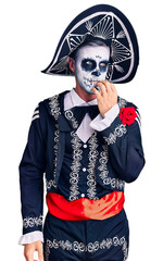 Wall Mural - Young man wearing day of the dead costume over background looking stressed and nervous with hands on mouth biting nails. anxiety problem.