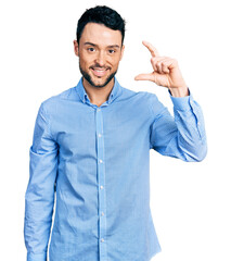 Canvas Print - Hispanic man with beard wearing casual business shirt smiling and confident gesturing with hand doing small size sign with fingers looking and the camera. measure concept.