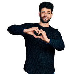 Wall Mural - Young arab man with beard wearing casual winter sweater smiling in love doing heart symbol shape with hands. romantic concept.