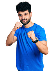 Poster - Young arab man with beard wearing casual blue t shirt ready to fight with fist defense gesture, angry and upset face, afraid of problem