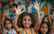 © imagineRbc - A young girl with curly hair smiles while raising her hand in a classroom setting, surrounded by other children participating in a lesson