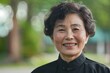© ChaoticMind - A smiling elderly woman is photographed outdoors wearing a black outfit, with blurred greenery in the background, showcasing her happiness and contentment.