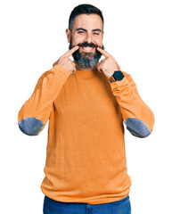 Wall Mural - Hispanic man with beard wearing casual winter sweater smiling with open mouth, fingers pointing and forcing cheerful smile