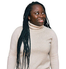 Canvas Print - Young black woman with braids wearing casual winter sweater looking away to side with smile on face, natural expression. laughing confident.