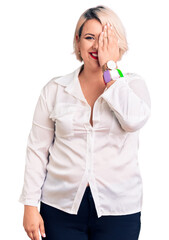 Wall Mural - Young blonde plus size woman wearing casual shirt covering one eye with hand, confident smile on face and surprise emotion.