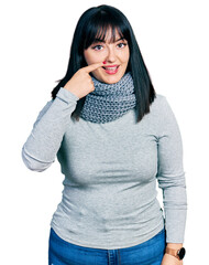 Sticker - Young hispanic plus size woman wearing winter scarf pointing with hand finger to face and nose, smiling cheerful. beauty concept