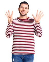 Sticker - Young handsome man wearing striped sweater showing and pointing up with fingers number nine while smiling confident and happy.