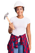 © Krakenimages.com - Young african american woman with braids wearing hardhat holding hammer looking positive and happy standing and smiling with a confident smile showing teeth