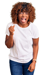 Poster - Young african american woman wearing casual white tshirt angry and mad raising fist frustrated and furious while shouting with anger. rage and aggressive concept.