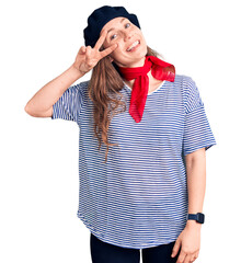 Wall Mural - Young beautiful blonde woman wearing french beret and striped t-shirt doing peace symbol with fingers over face, smiling cheerful showing victory