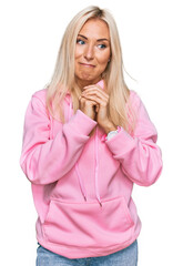 Poster - Young blonde woman wearing casual sweatshirt laughing nervous and excited with hands on chin looking to the side