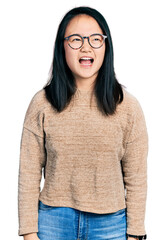 Wall Mural - Young chinese woman wearing casual sweater and glasses angry and mad screaming frustrated and furious, shouting with anger. rage and aggressive concept.