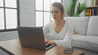 © Krakenimages.com - A focused young woman using a laptop in a modern living room with natural light and minimalistic decor.