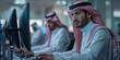 © Georgii - Focused Saudi Arabian men working on computers in an office environment wearing traditional attire
