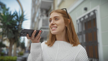 Wall Mural - A young woman using her smartphone for a voice message on a lively urban street.