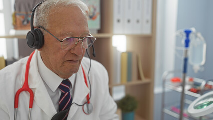 Canvas Print - An elderly caucasian man with grey hair, wearing a headset and a stethoscope, works in a hospital clinic office, illustrating a healthcare professional in his indoor workplace.