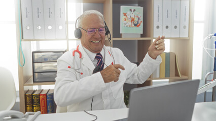 Poster - Elderly, caucasian, man, in, a, clinic, workplace, with, grey, hair, using, a, laptop, and, wearing, headphones, while, smiling.