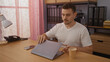 © Krakenimages.com - A handsome young hispanic man with a beard, wearing a white shirt, working on a laptop in a modern office with pink curtains and organized shelves in the background.