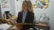 © Krakenimages.com - Young blonde woman detective analyzing documents in a police station office, depicting concentration and investigation.
