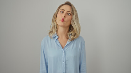 Wall Mural - Playful young caucasian woman puckering lips in blue shirt against isolated white background.