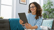 © Krakenimages.com - Smiling woman with curly hair wearing glasses and blue sweater using a tablet in a cozy living room